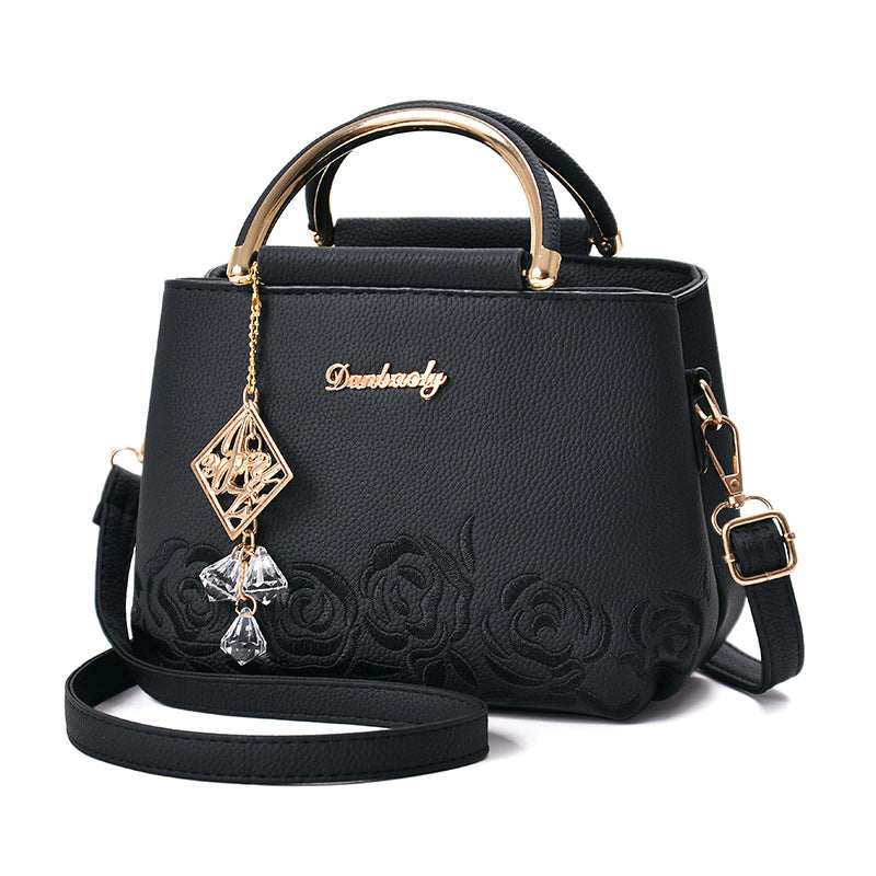 Black handbag with floral embroidery and decorative chain on a white background